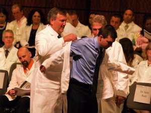 Nate Kauffman receiving white coat by two doctors at ceremony